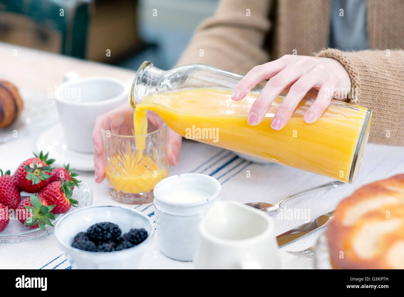 Cropped view of woman pouring orange juice from bottle into glass Stock Photo