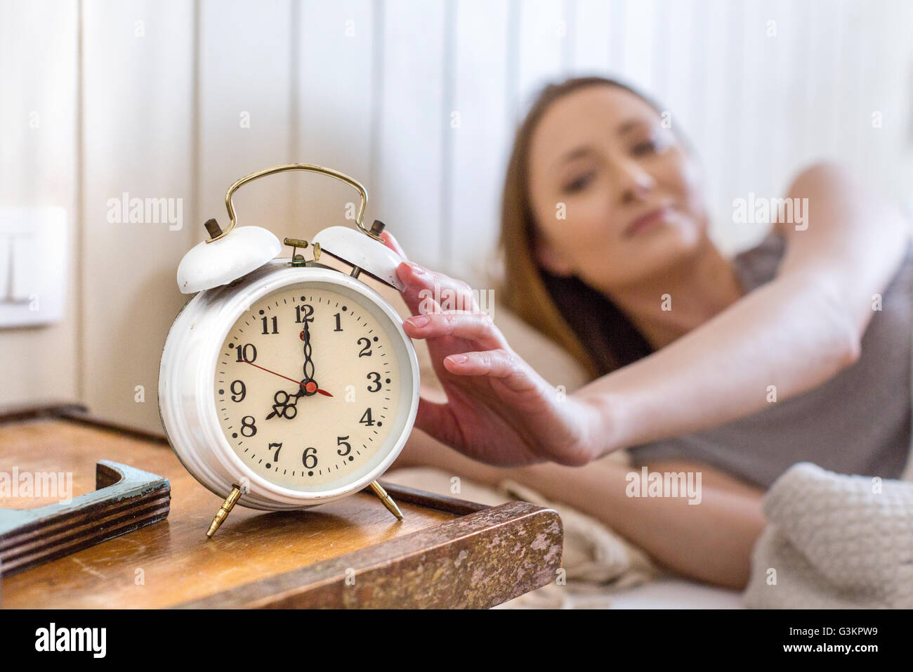 Woman in bed reaching for alarm clock on bedside table Stock Photo Alamy