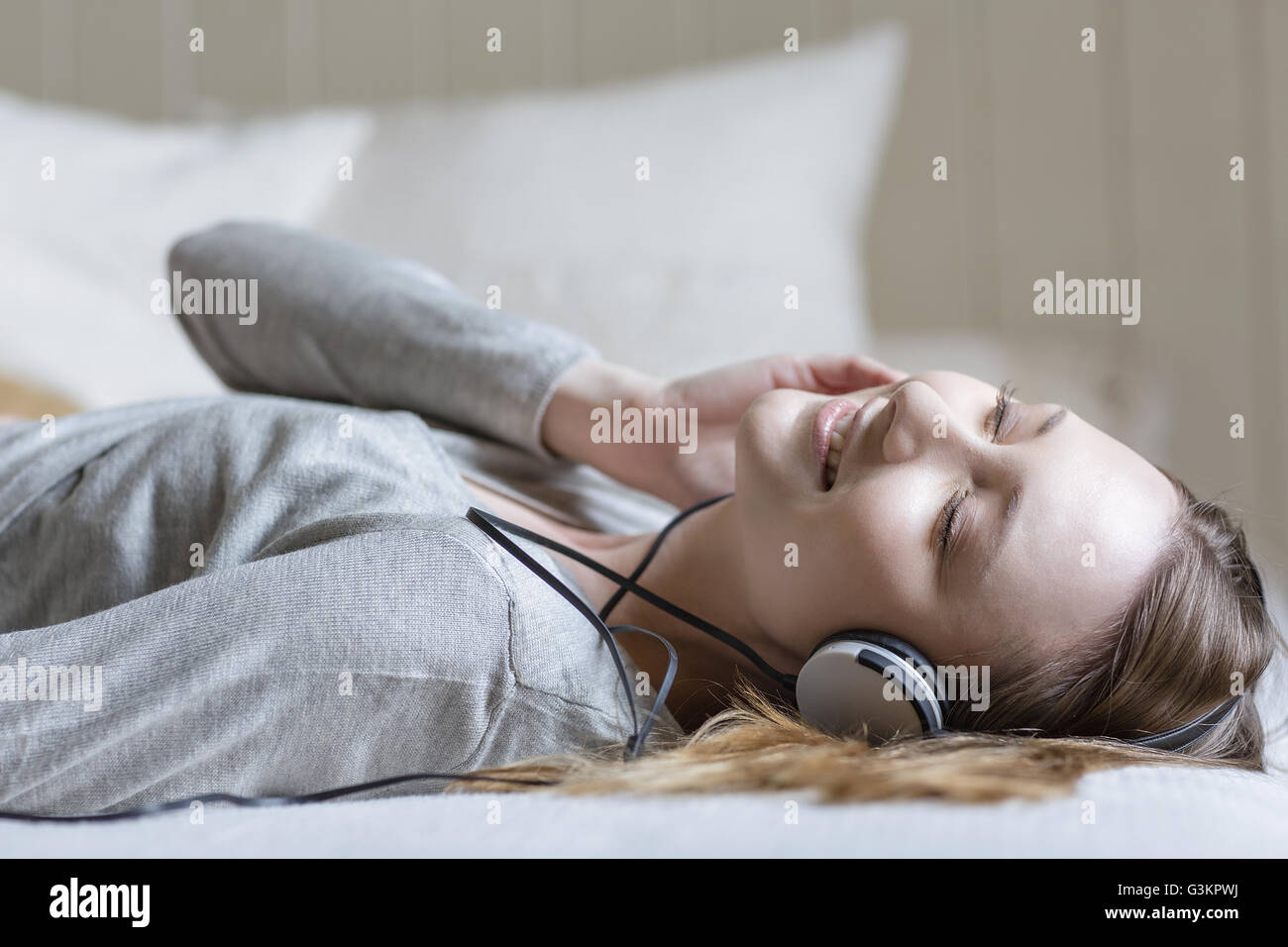 Woman lying on bed wearing head phones, eyes closed smiling Stock Photo ...