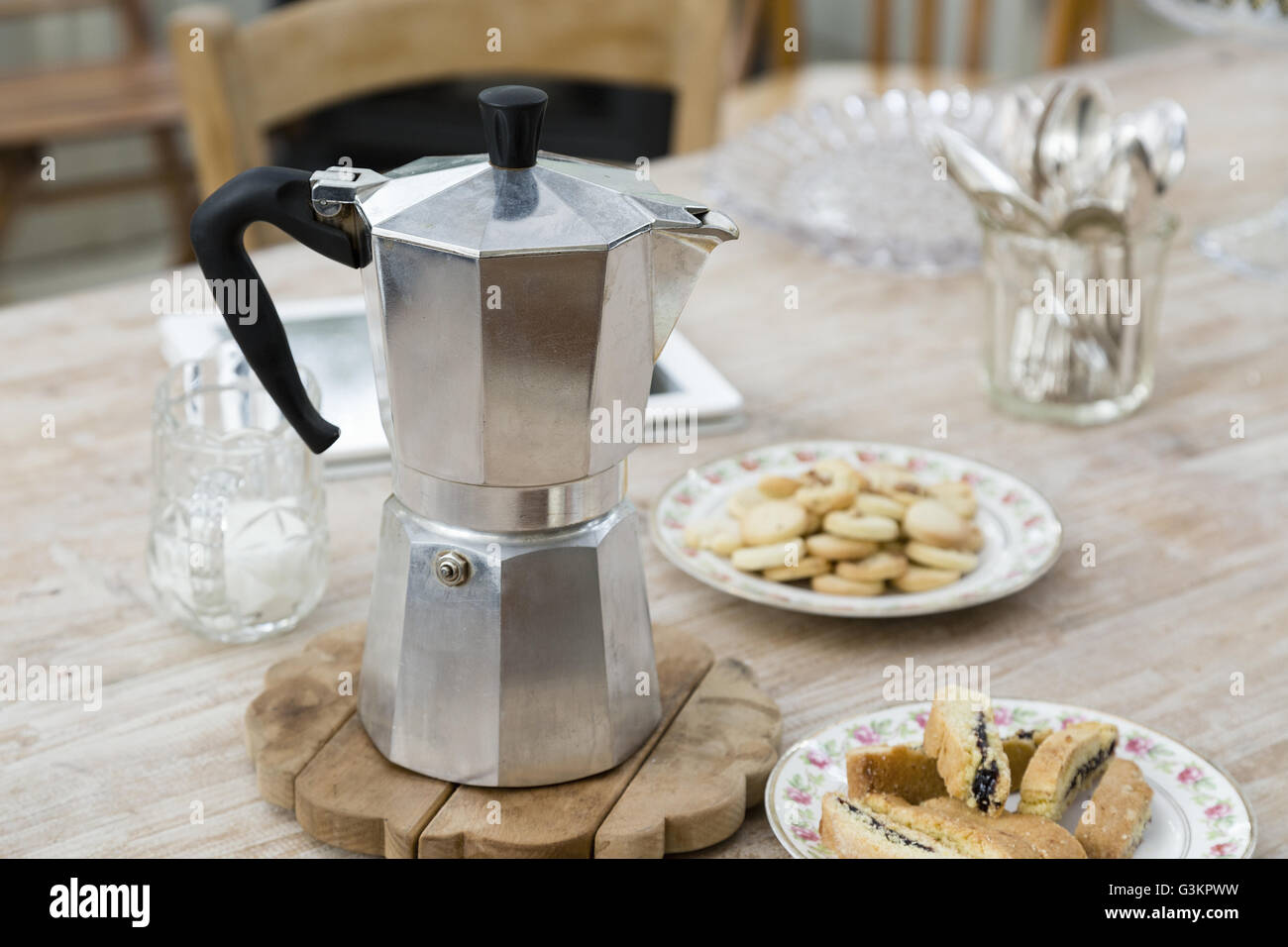 Stove top coffee pot with plates of baked good on dining table Stock