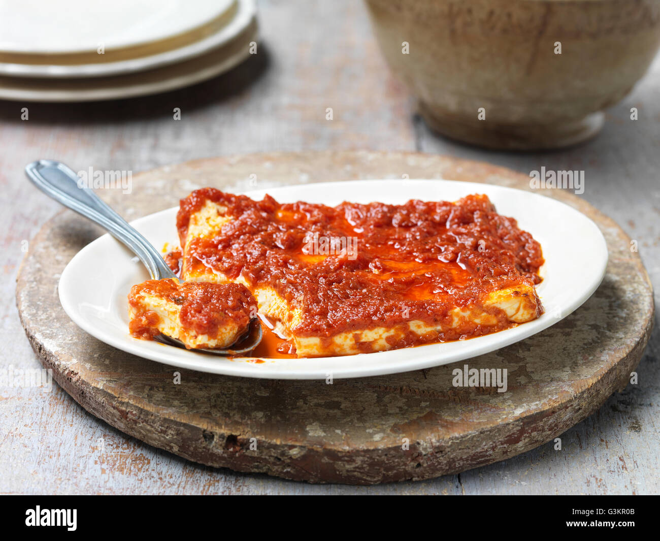 Baked feta cheese with sun dried tomato sauce, in bowl with spoon Stock Photo