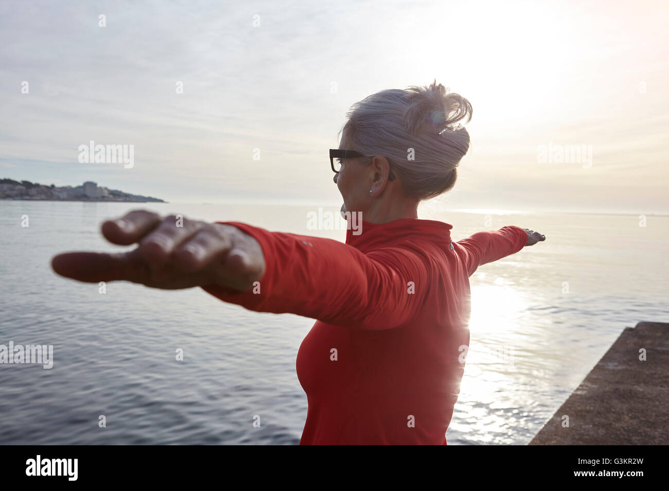 Mature woman standing beside water, in yoga position, rear view Stock ...