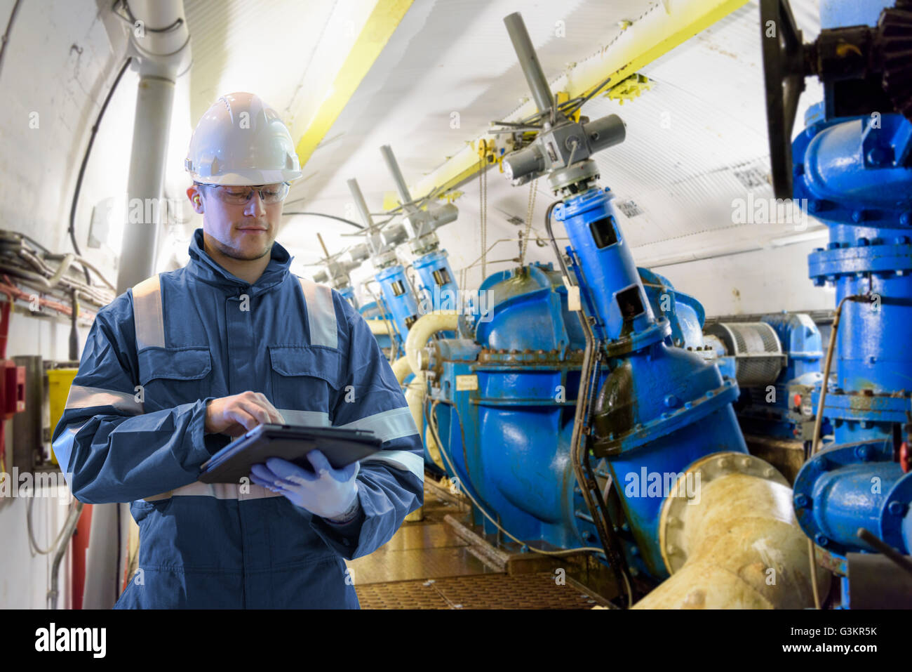 Worker using digital tablet to take readings in straining gallery in hydroelectric power station Stock Photo