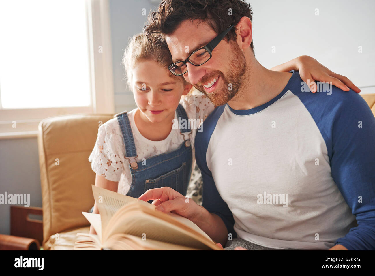 Mid adult man reading book with daughter on sofa Stock Photo