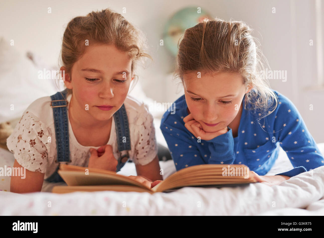 Two sisters lying on bed reading a book Stock Photo