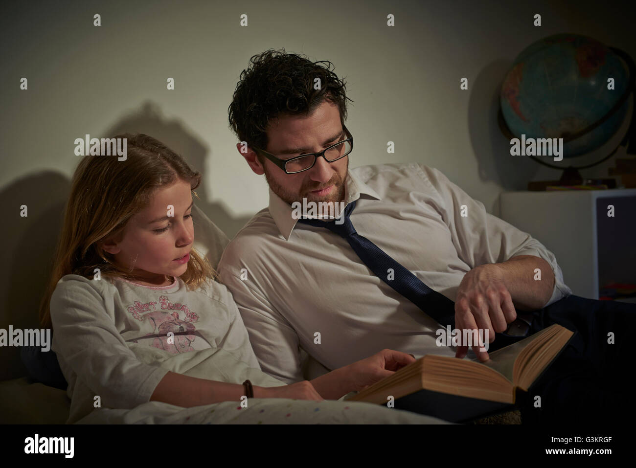 Businessman reading storybook to daughter at bedtime Stock Photo