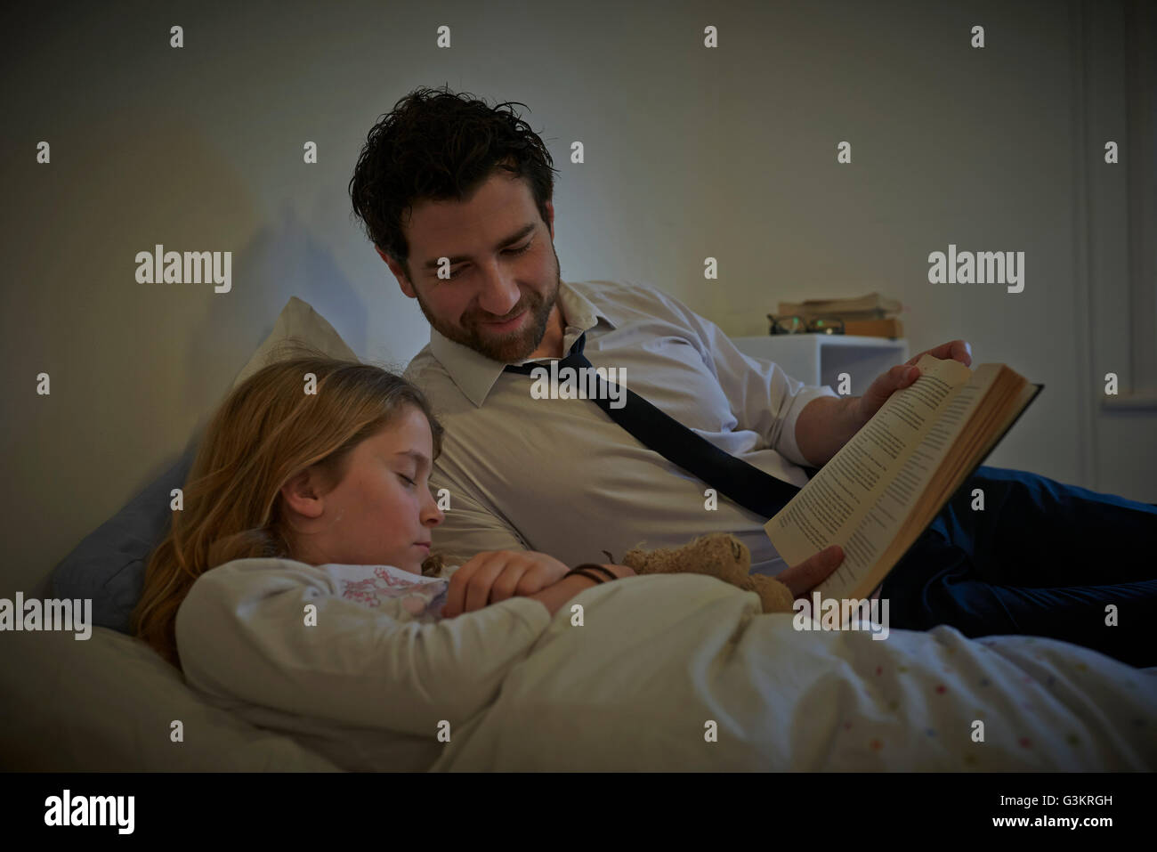Businessman reading storybook to sleeping daughter at bedtime Stock Photo