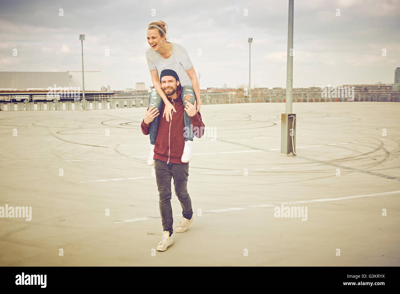 Mid adult man giving shoulder ride to girlfriend on rooftop parking lot ...