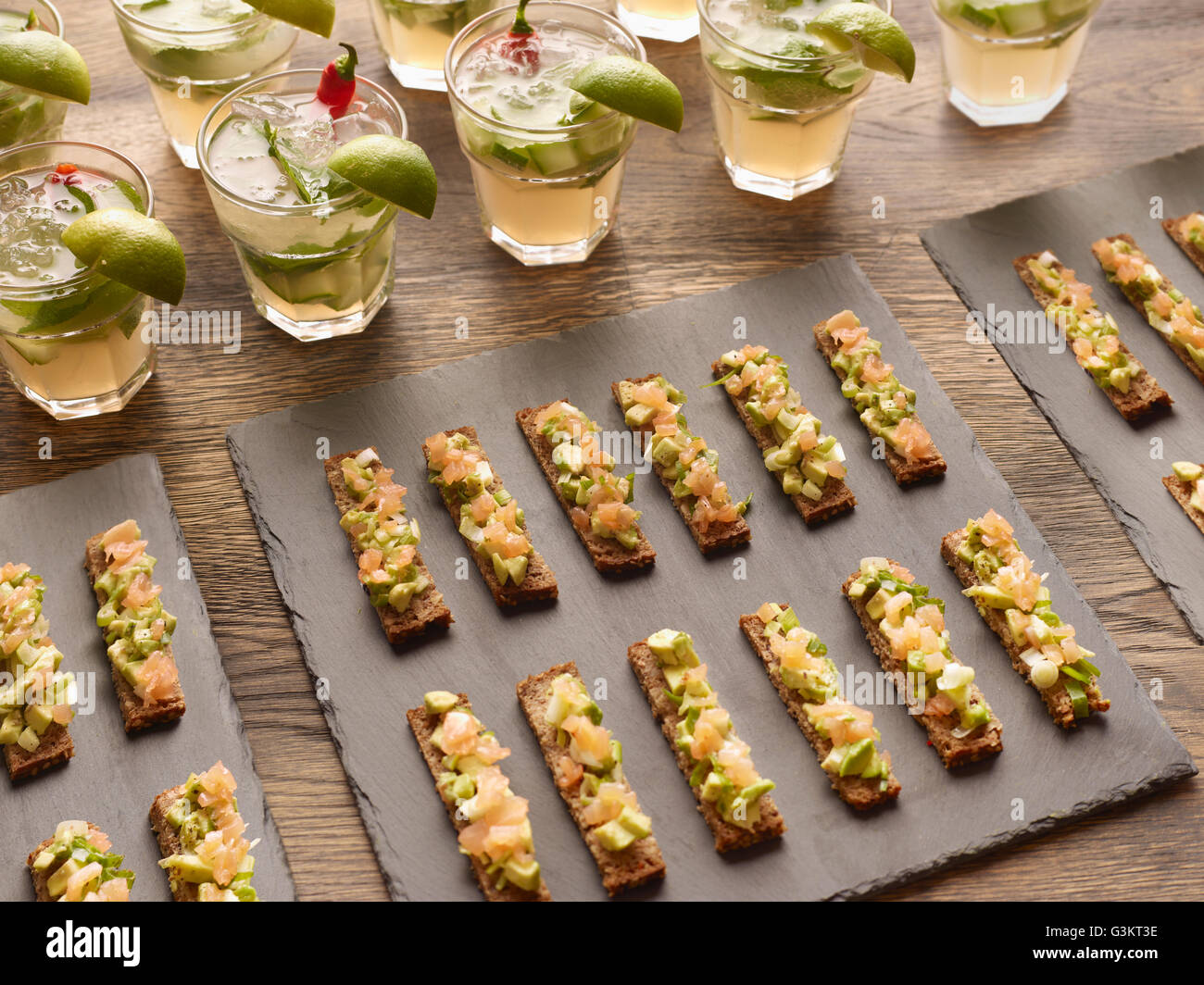 Guacamole, smoked salmon and rye bread canapes with vodka cocktail garnished with lime wedges Stock Photo