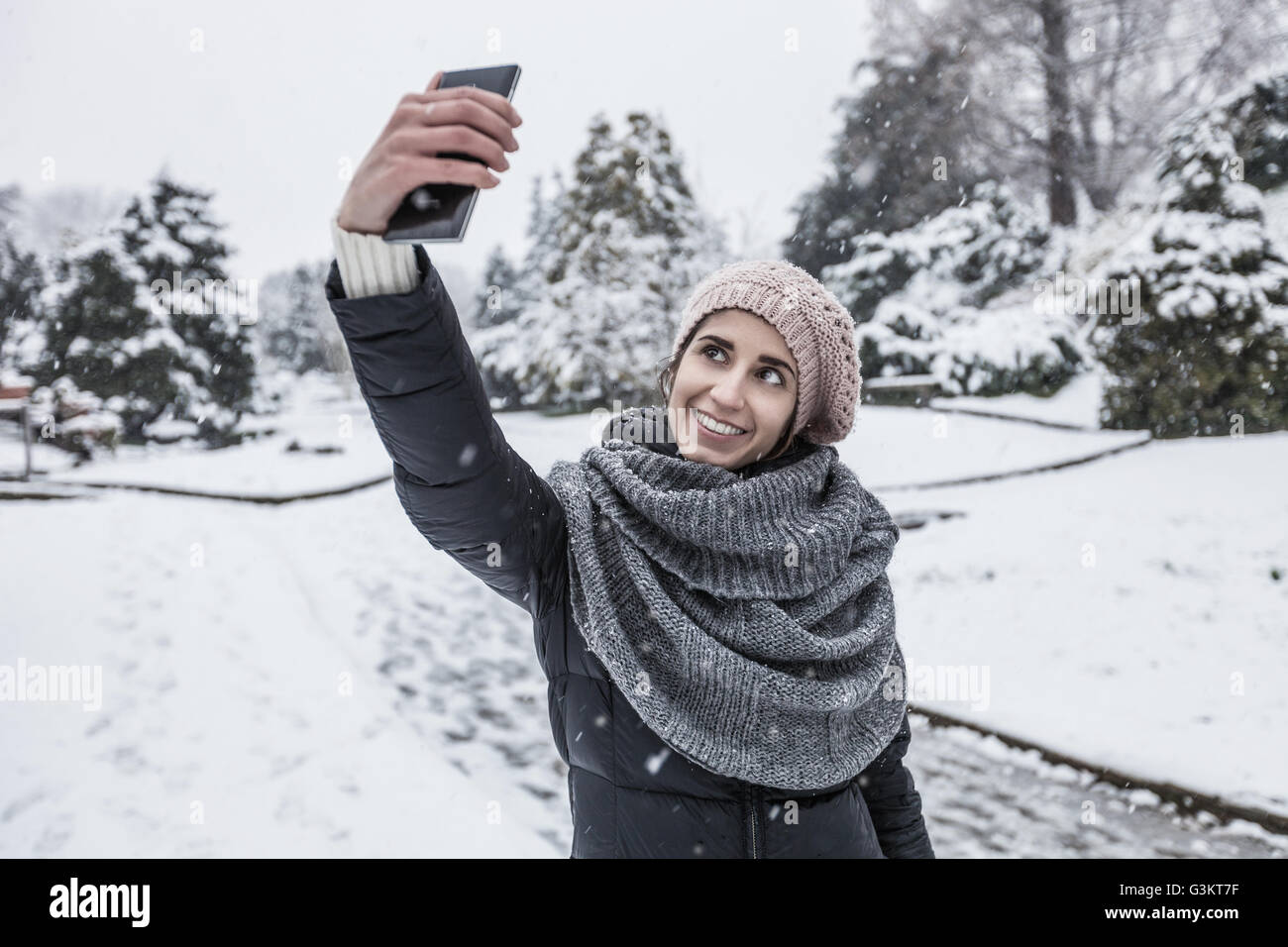 Woman on snow covered landscape using smartphone to take selfie Stock Photo