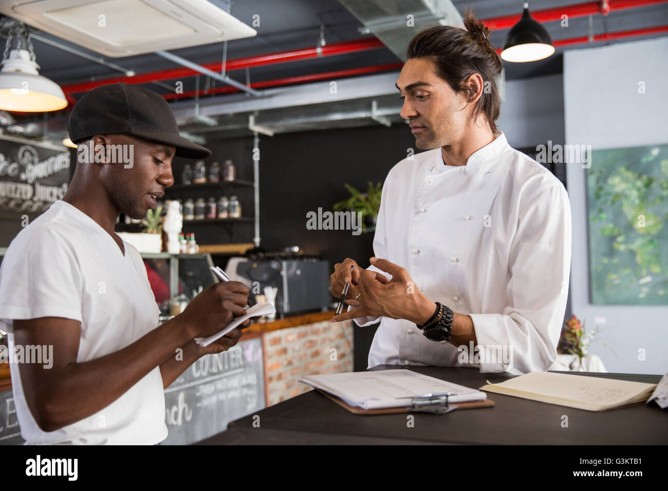 Employee in restaurant talking with chef, making notes in notebook Stock Photo