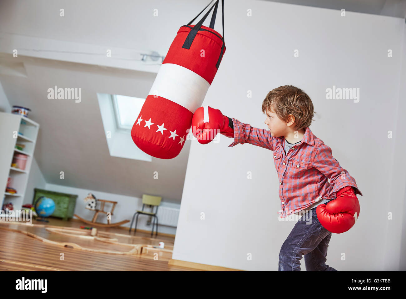 Boy wearing boxing gloves punching punch bag Stock Photo