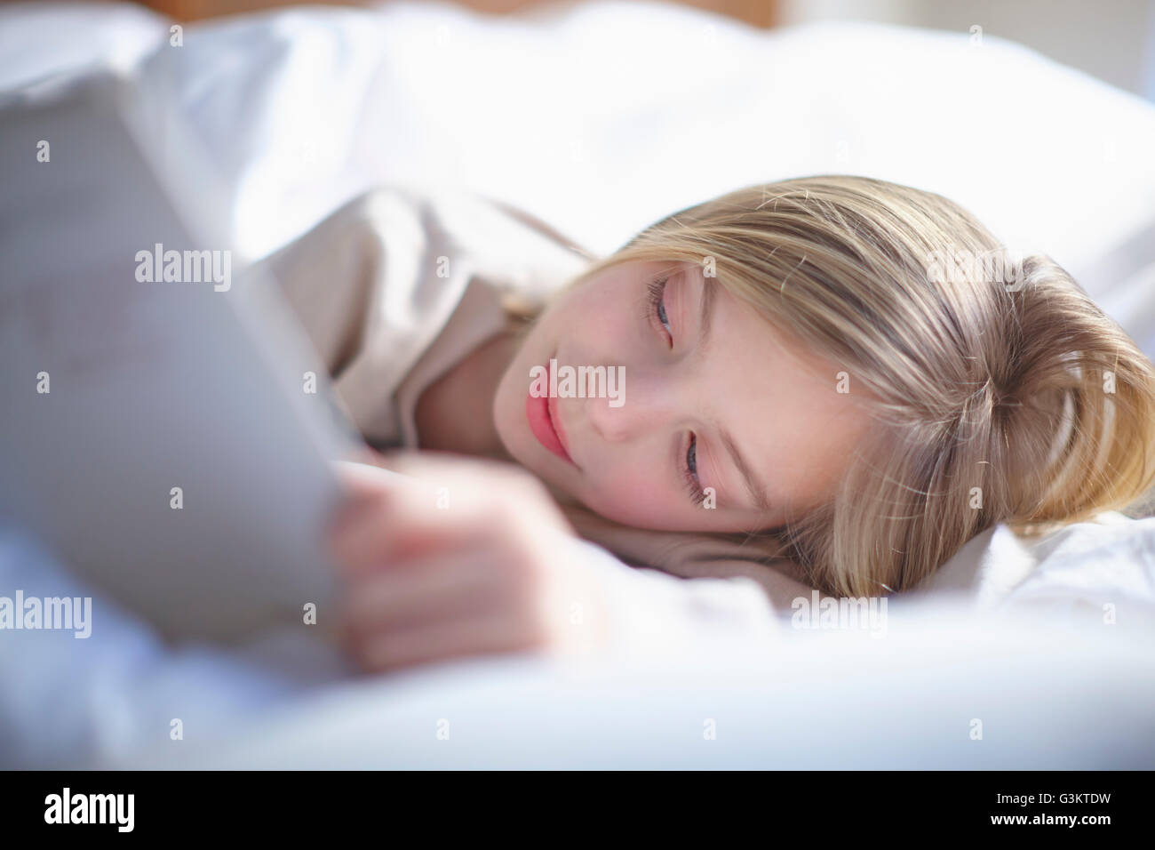 Blond haired girl lying in bed reading a book Stock Photo