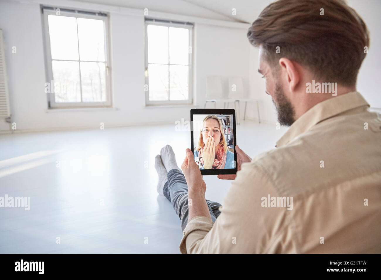 Girlfriend on digital tablet video call blowing a kiss to young man sitting on floor Stock Photo