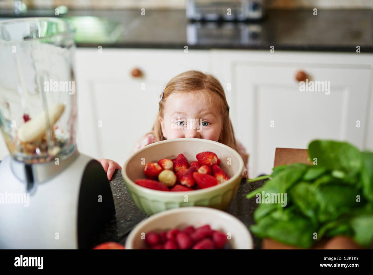 Girl peeking over bowls of strawberries of kitchen counter Stock Photo