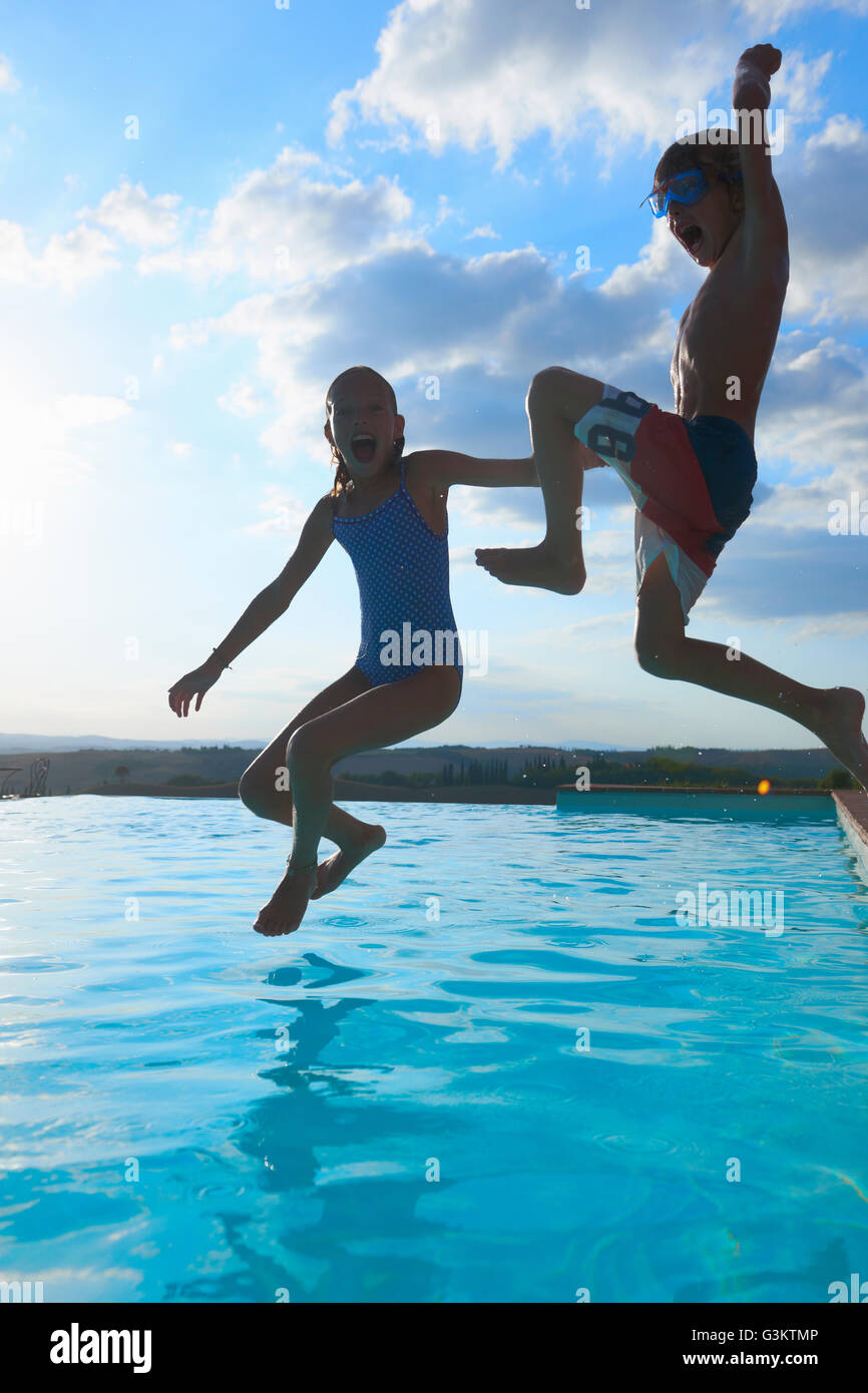Girl and brother jumping into swimming pool, Buonconvento, Tuscany, Italy Stock Photo