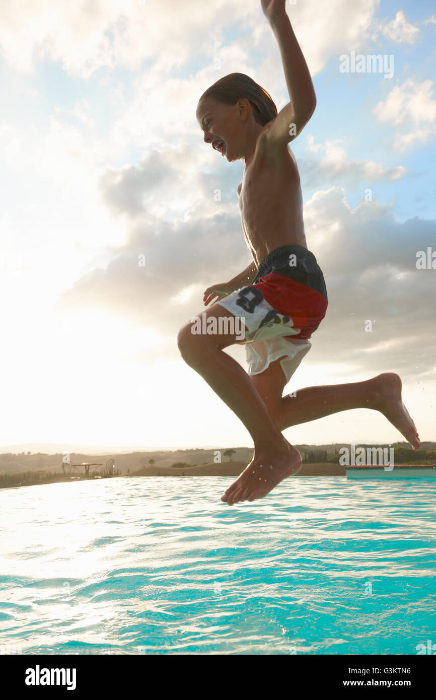 Boy jumping mid air into swimming pool, Buonconvento, Tuscany, Italy Stock Photo