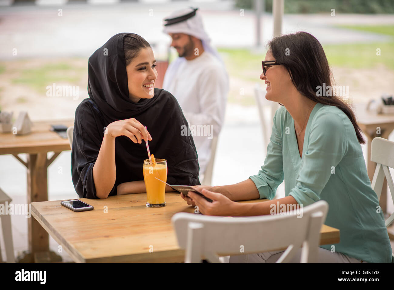 Young middle eastern woman wearing traditional clothing talking with female friend at cafe, Dubai, United Arab Emirates Stock Photo