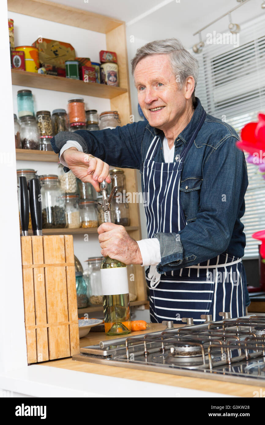 Man opening bottle of wine in kitchen Stock Photo