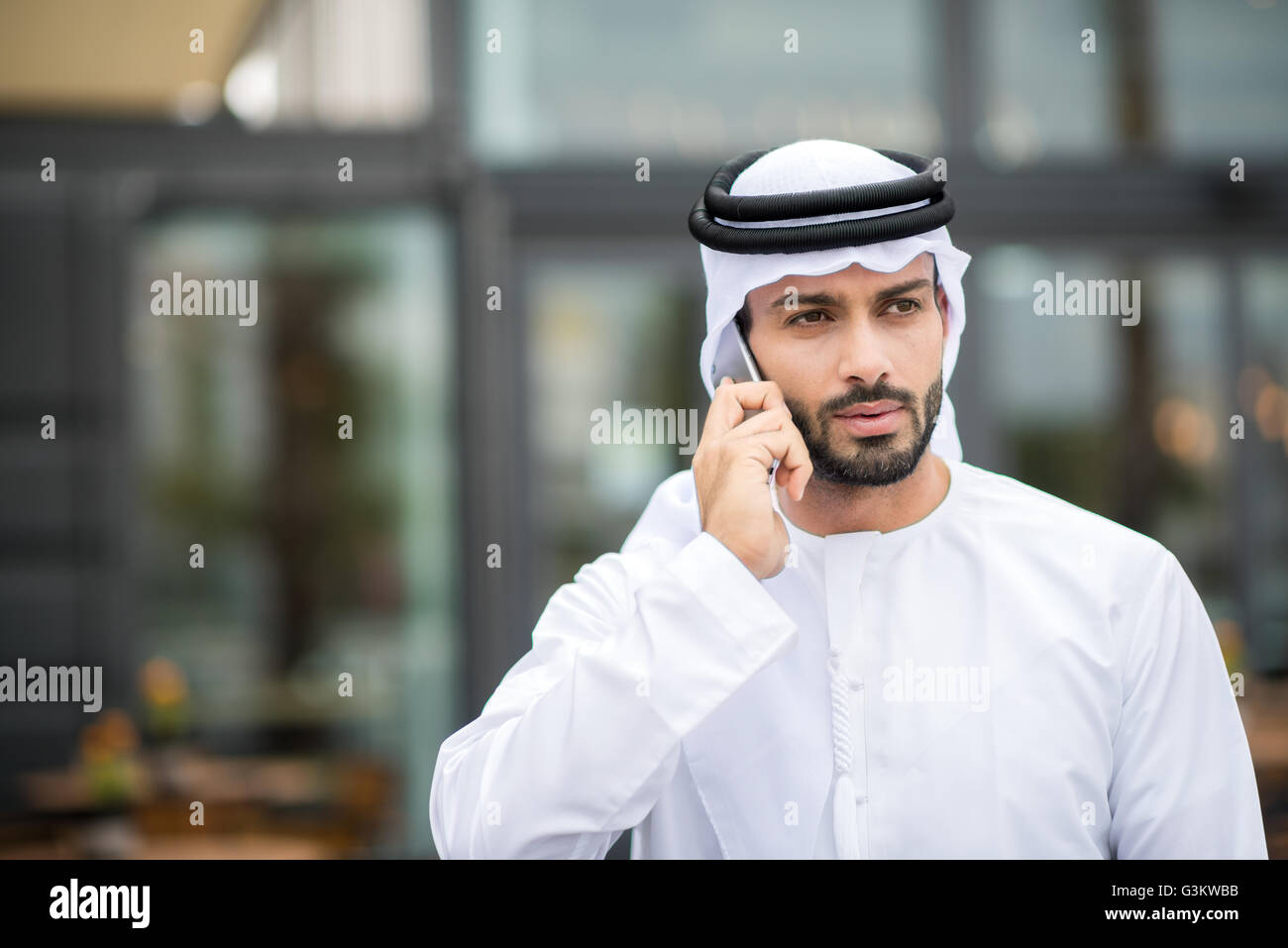 Man wearing dishdasha walking along street talking on smartphone, Dubai, United Arab Emirates Stock Photo