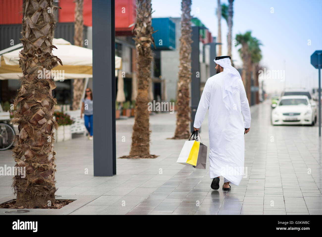 Rear view of man wearing dishdasha walking along street carrying shopping bags, Dubai, United Arab Emirates Stock Photo