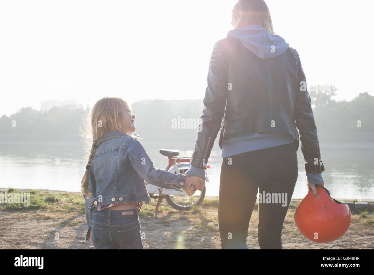 Mother and daughter, holding hands, beside lake, rear view Stock Photo