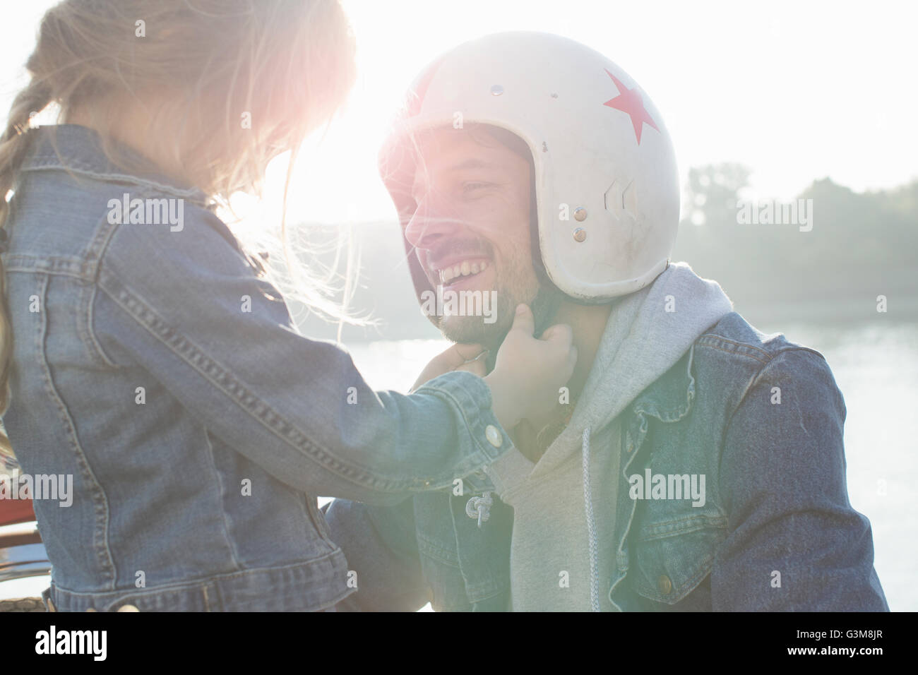 Young girl helping her father put on crash helmet Stock Photo