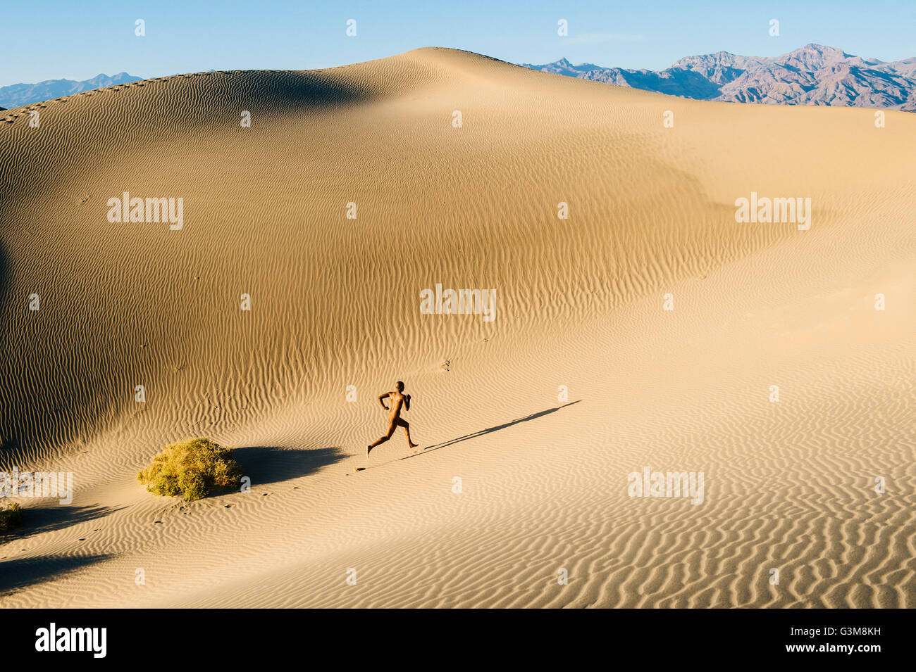Nude woman in desert running up dune Stock Photo