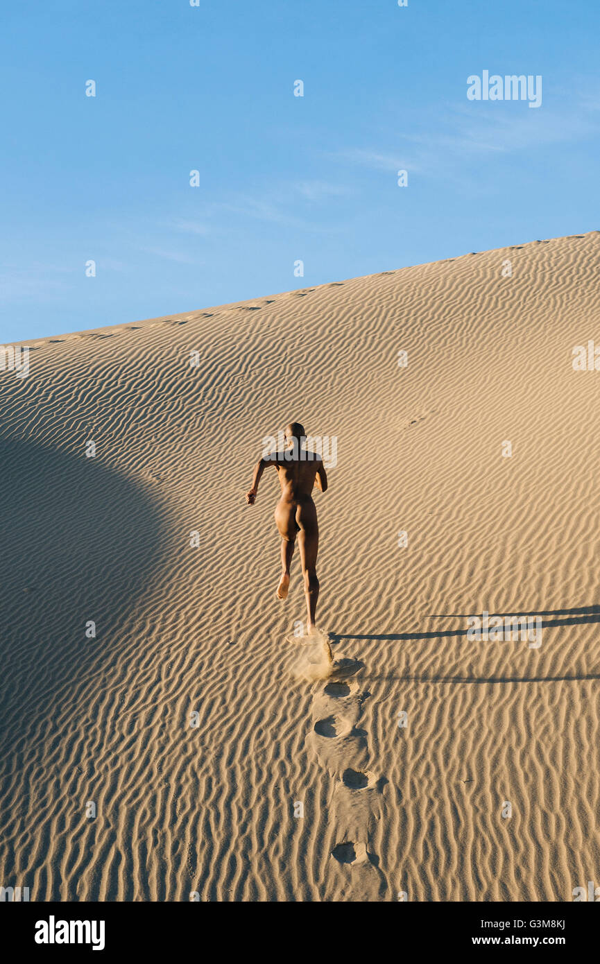Nude woman running in desert leaving footprints Stock Photo
