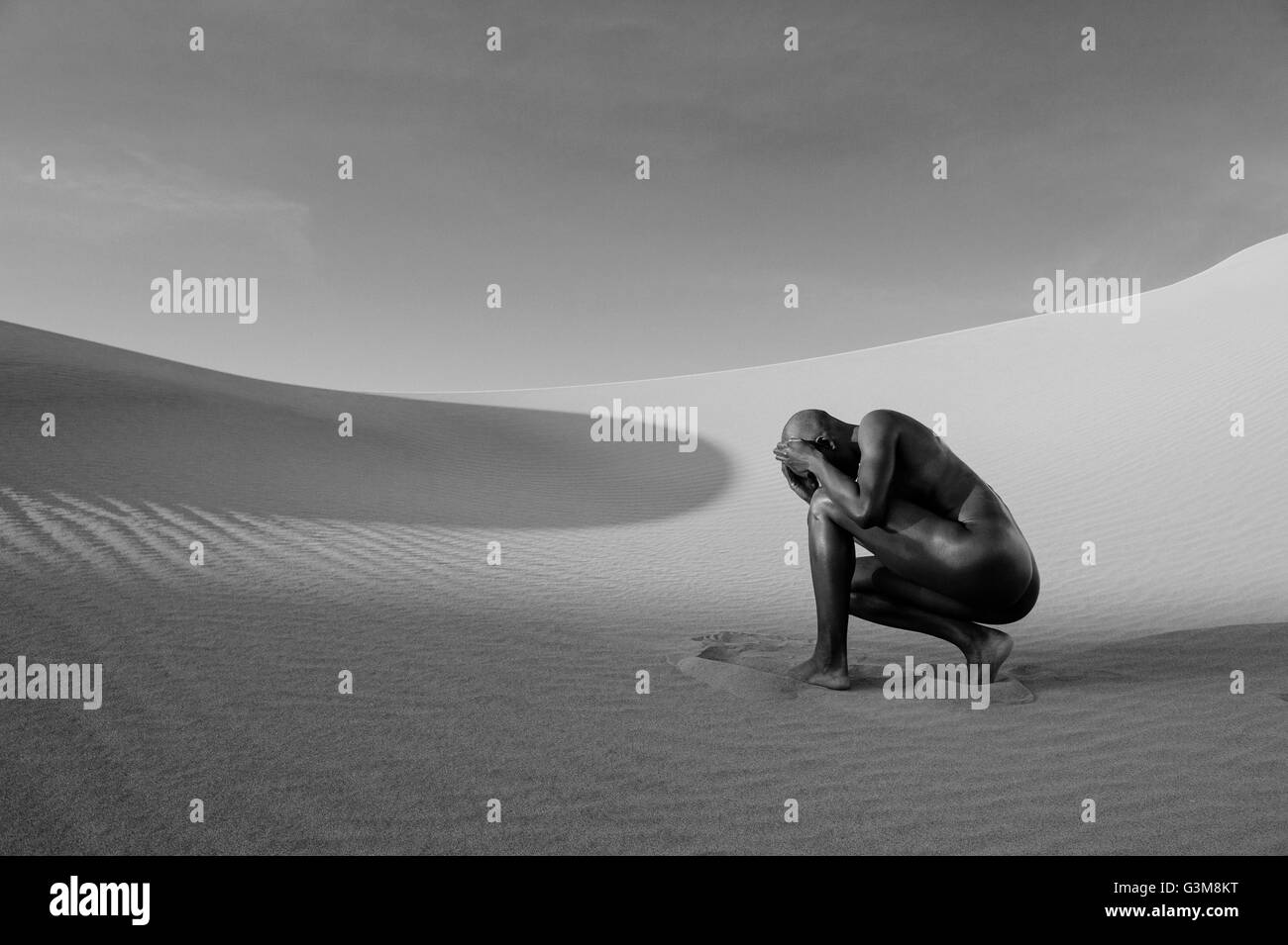 Nude woman cowering in desert Stock Photo