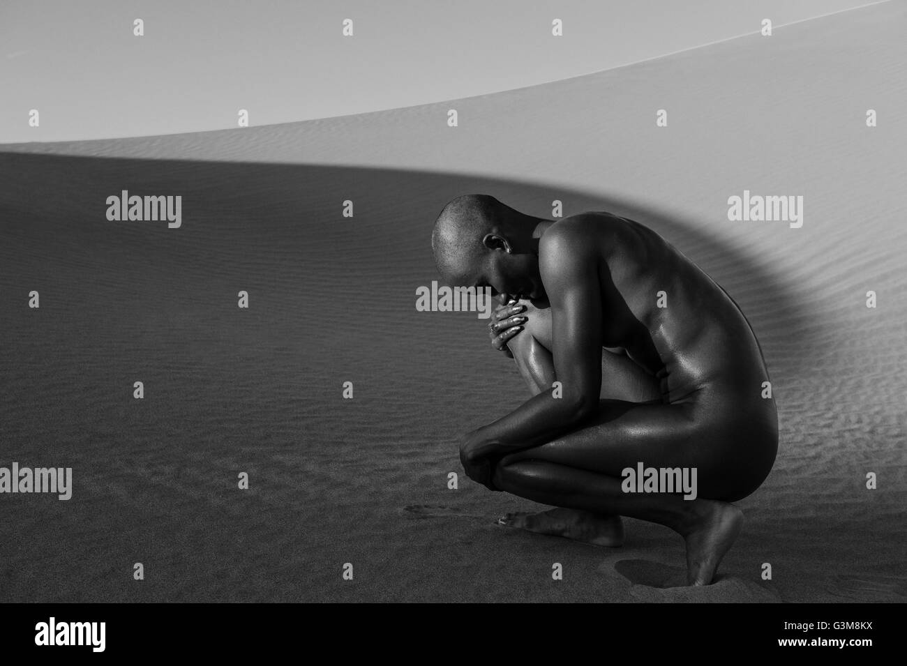Nude woman crouching in desert Stock Photo