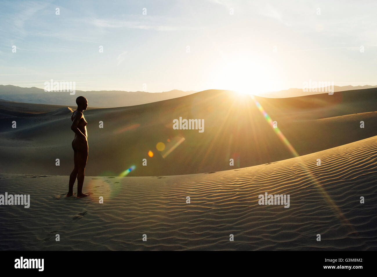 Nude woman in desert on sand dune looking away Stock Photo