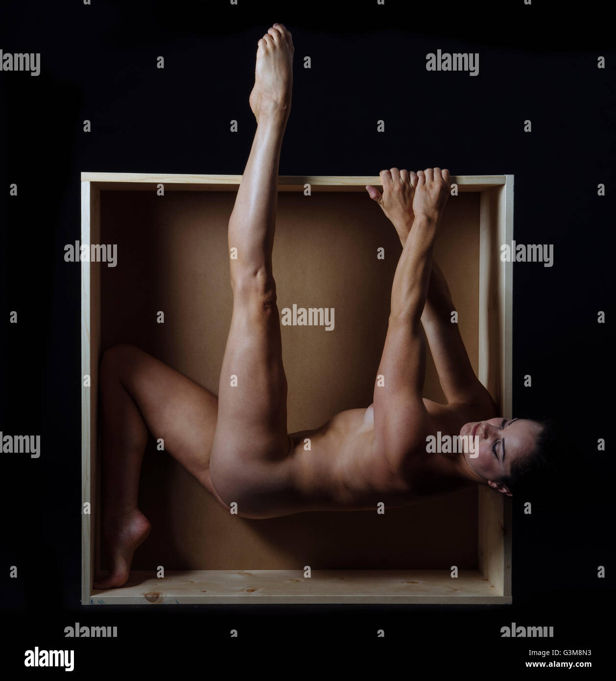 Naked woman hanging from edge of box Stock Photo