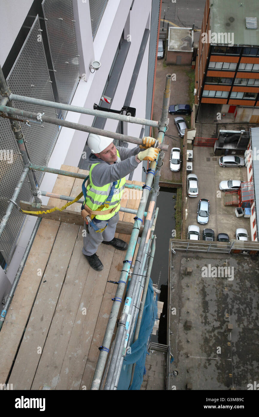 A scaffolder builds a temporary work platform near the top of a tall tower block in Birmingham. Shows city street far below. Stock Photo
