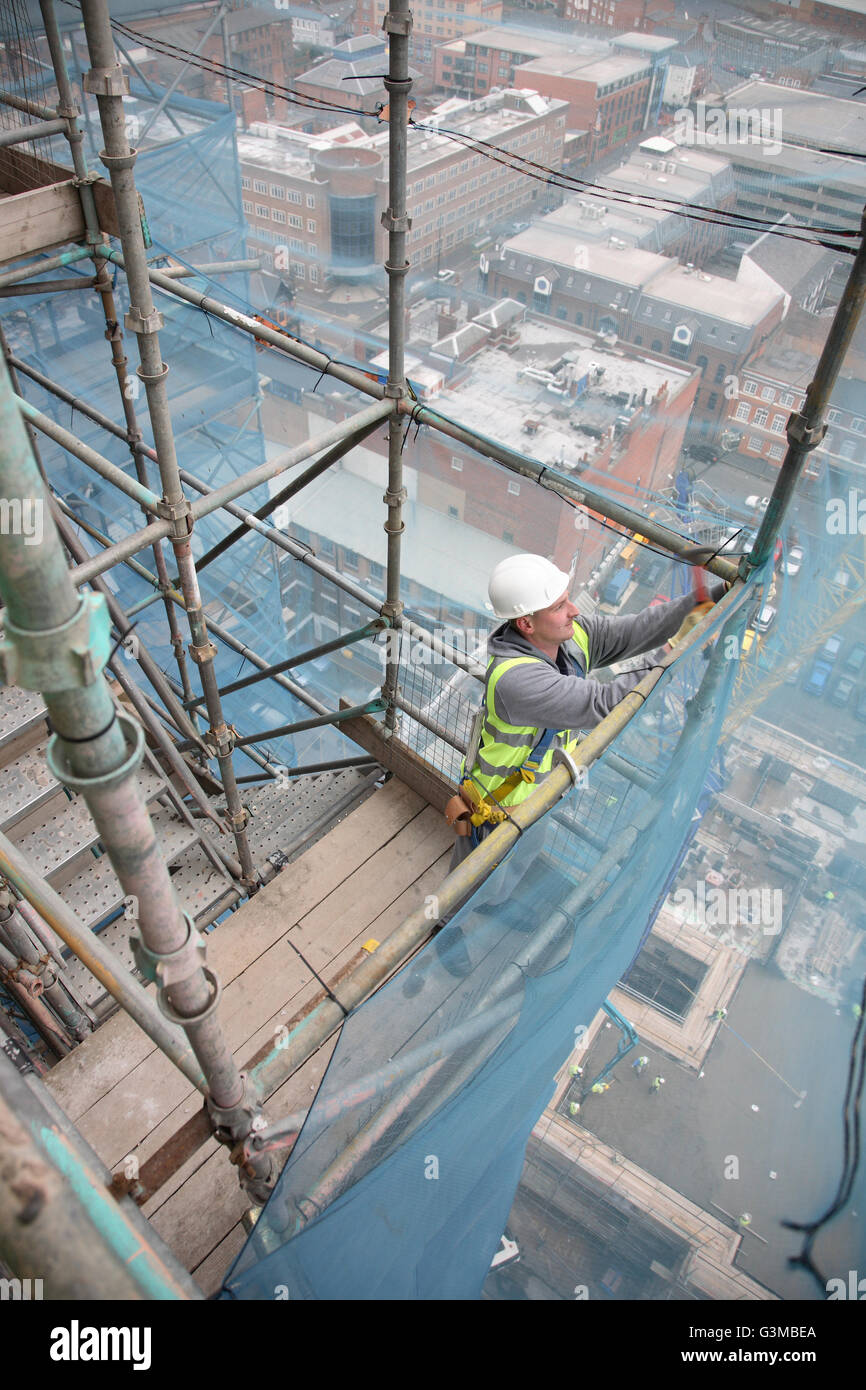 A scaffolder works on a temporary staircase near the top of a tall tower block in Birmingham. Shows city centre far below. Stock Photo