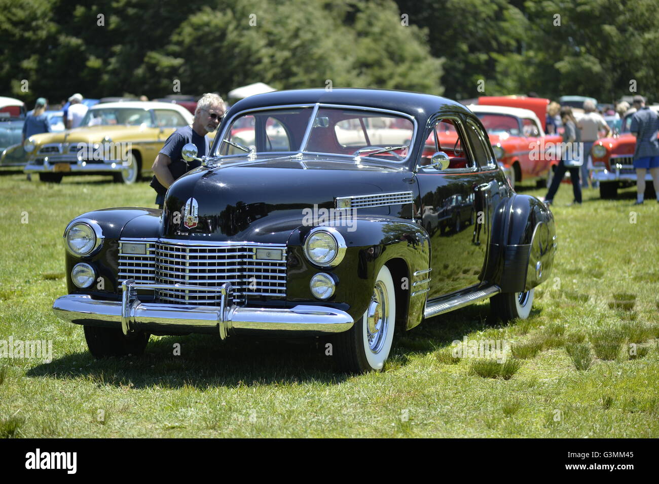 Westbury, New York, USA. June 12, 2016.  Visitor looks at interior of black vintage Cadillac with front chrome grille and bumpers and white wall tires is on display at the Antique and Collectible Auto Show at the 50th Annual Spring Meet at Old Westbury Gardens, in the Gold Coast of Long Island, and sponsored by Greater New York Region, GNYR, Antique Automobile Club of America, AACA. Participating vehicles in the judged show included hundreds of domestic and foreign, antique, classic, collectible, and modern cars. Stock Photo