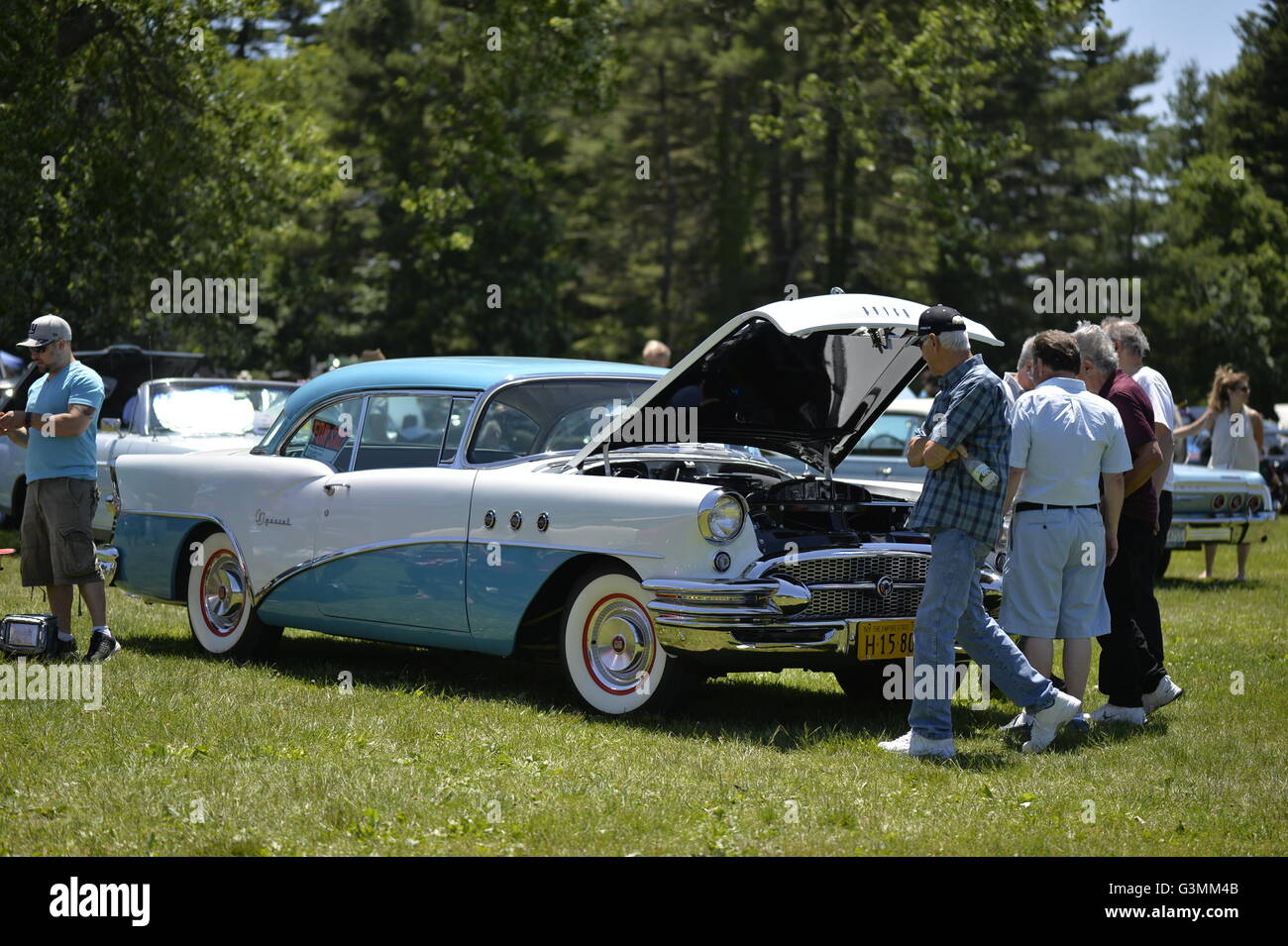 Westbury, New York, USA. June 12, 2016. Visitors are examining engine under the open hood of turquois and white 1955 Buick Special, owned by Rick D'Alessandro of Masapequa, at the Antique and Collectible Auto Show at the 50th Annual Spring Meet at Old Westbury Gardens, in the Gold Coast of Long Island, and sponsored by Greater New York Region, GNYR, Antique Automobile Club of America, AACA. Participating vehicles in the judged show included hundreds of domestic and foreign, antique, classic, collectible, and modern cars. Stock Photo