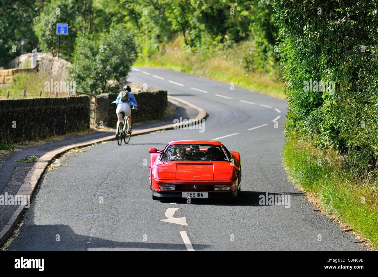 Ferrari Testarossa driving along a country road on a summer's day, passing a cycling going in the opposite direction Stock Photo