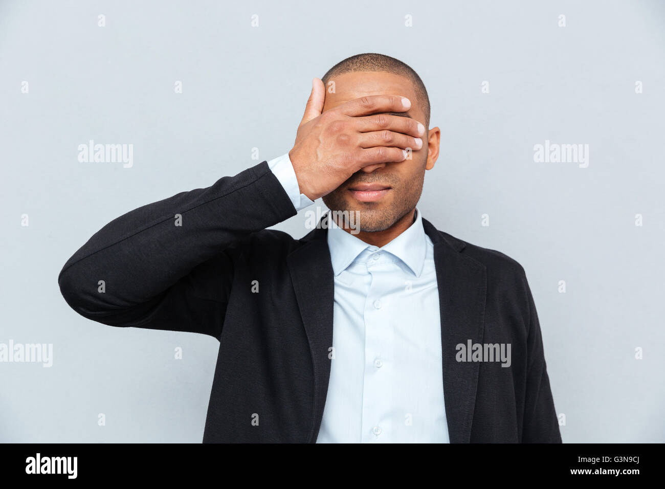 Portrait of a businessman covering eyes isolated on gray background Stock Photo