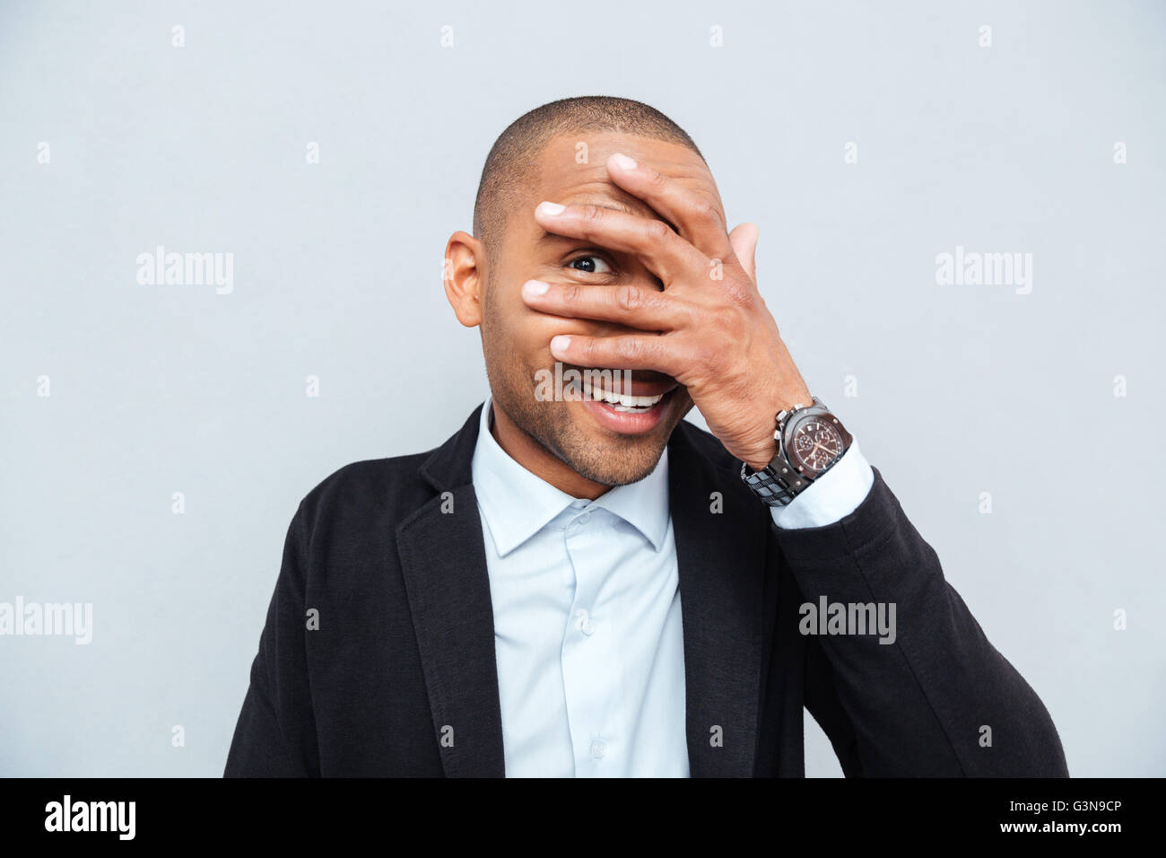 Young businessman hiding eyes behind his hand isolated on gray