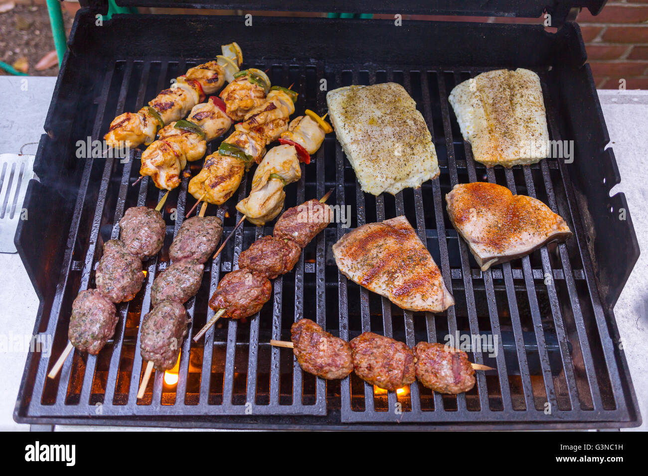 VIRGINIA, USA - Chicken kabobs, lamb kofta skewers, and fish grilling on barbecue. Stock Photo