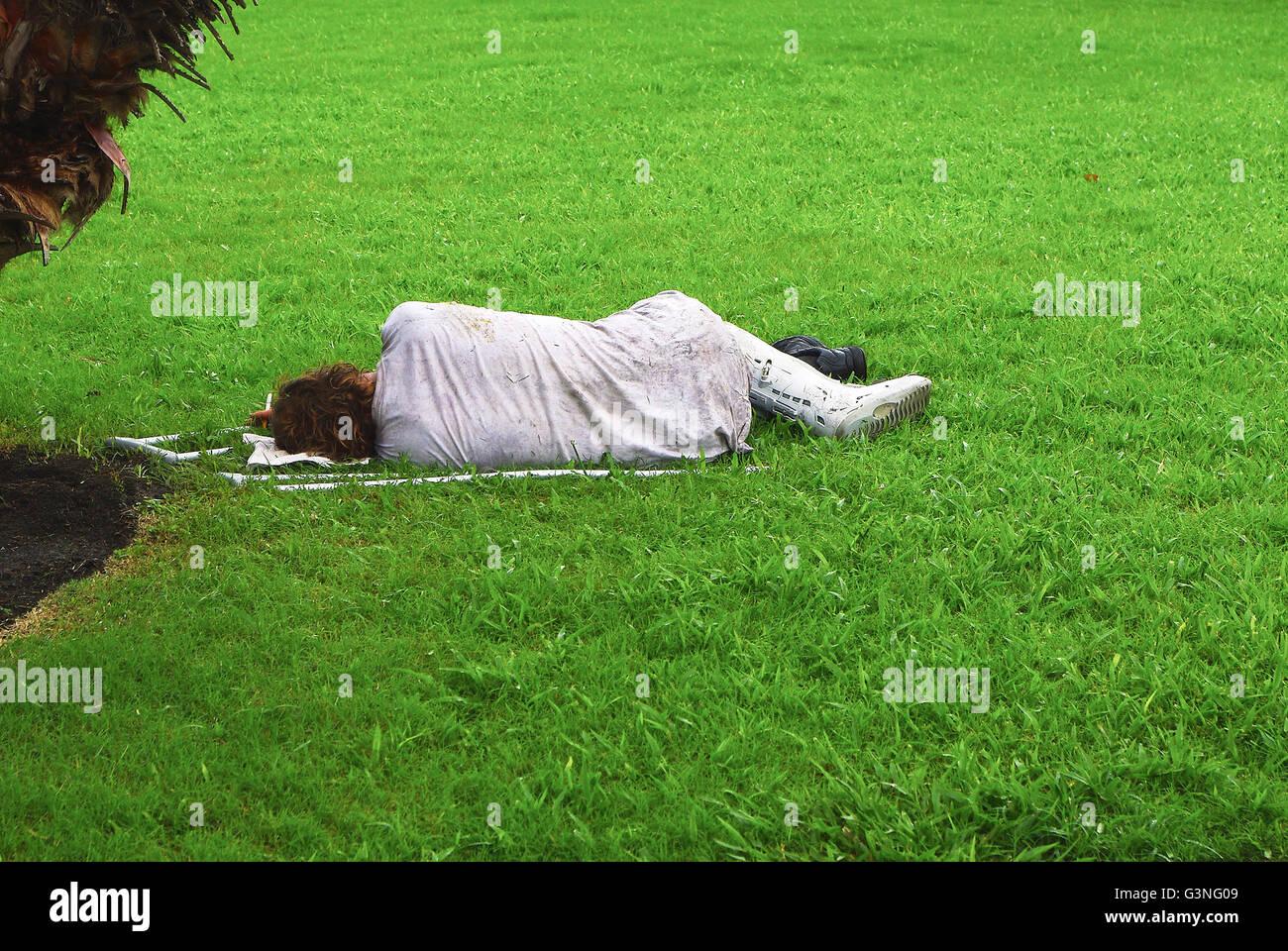 Homeless? man with broken leg sleeping on the grass with lit sigarette Stock Photo