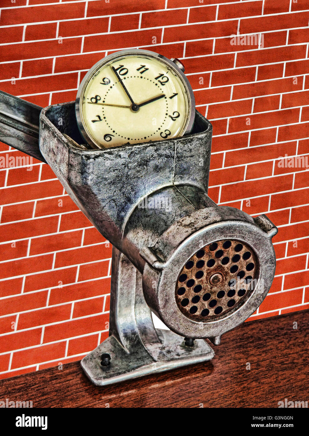 Alarm clock in meat grinder on red brick wall background taken closeup. Stock Photo