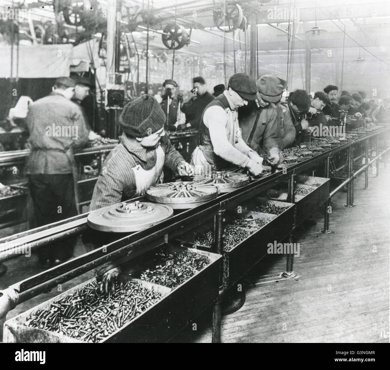These workers in 1913 at the Ford Motor Company plant made industrial history by building a flywheel magneto on a moving assembly line. Here they are on the assembly line. Stock Photo