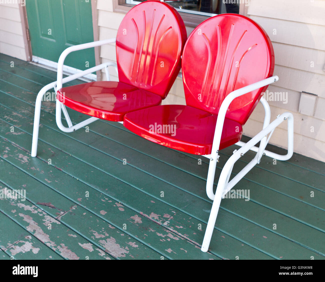 Mid-century red two-seater bench on a worn wooden front port Stock Photo