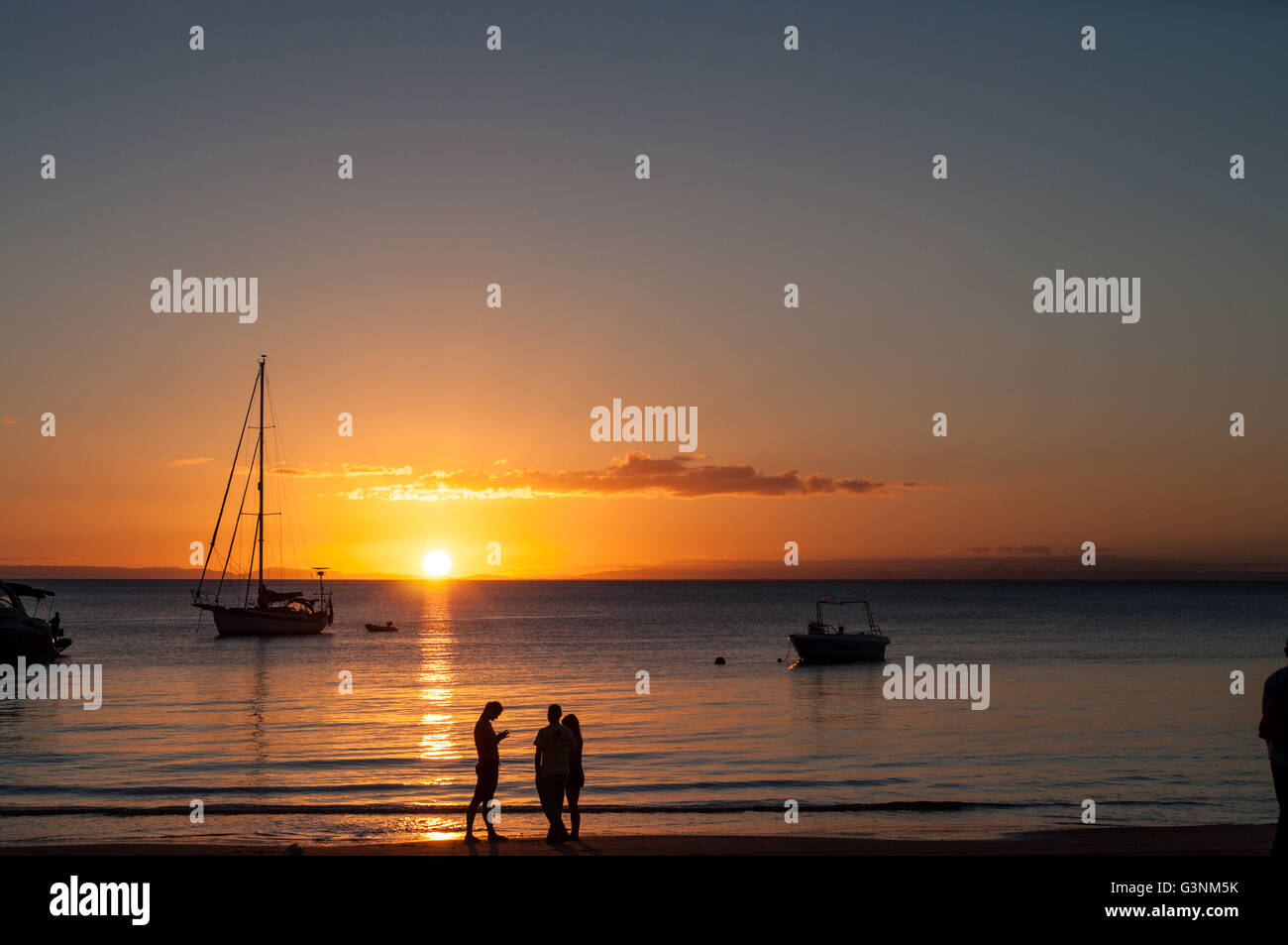 sunset at a beach shore with boats on the water and silhouettes of ...
