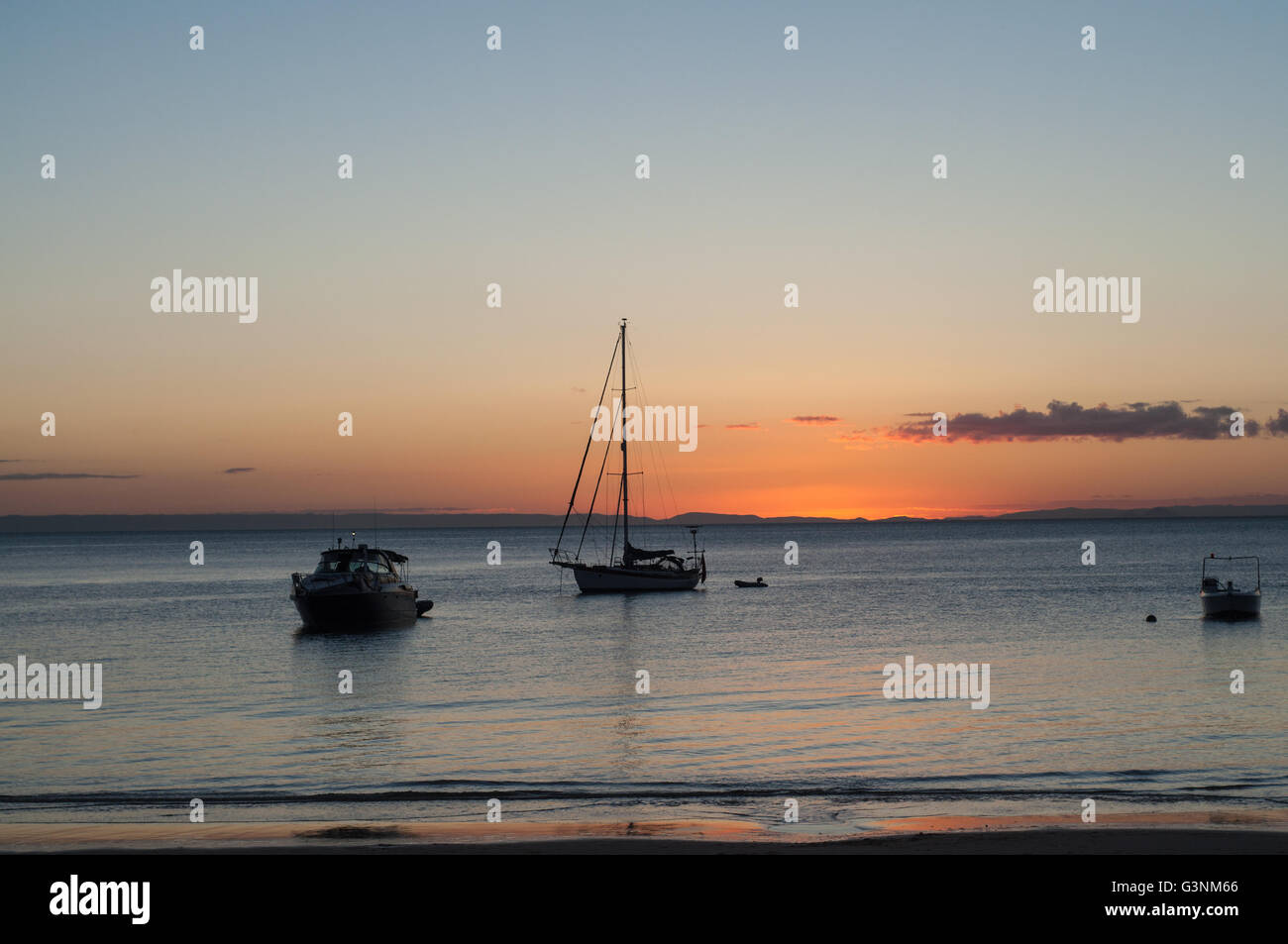 sunset at a beach shore with boats on the water Stock Photo - Alamy