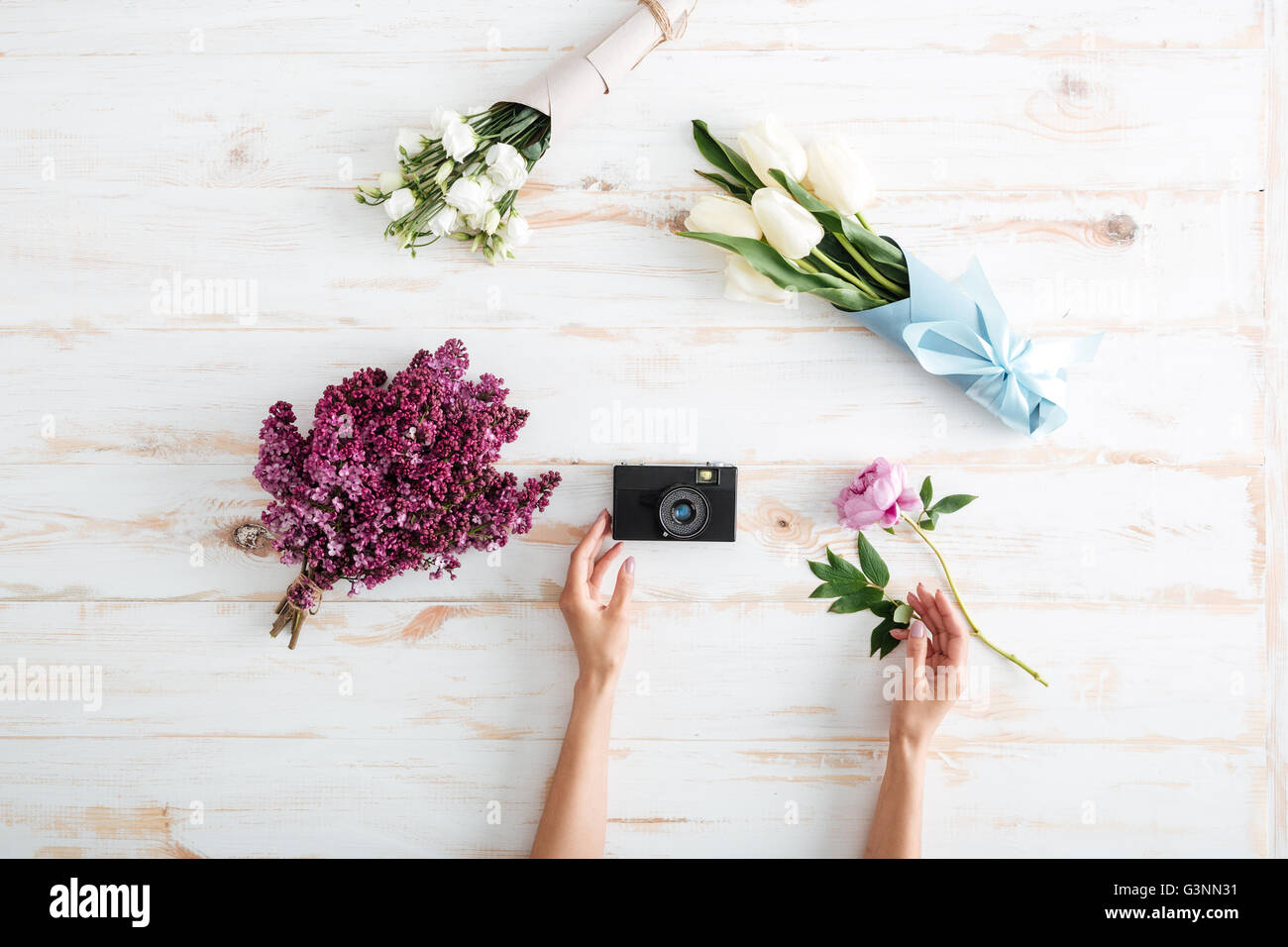 Hands of young woman put flower bouquets and photo camera on wooden table Stock Photo