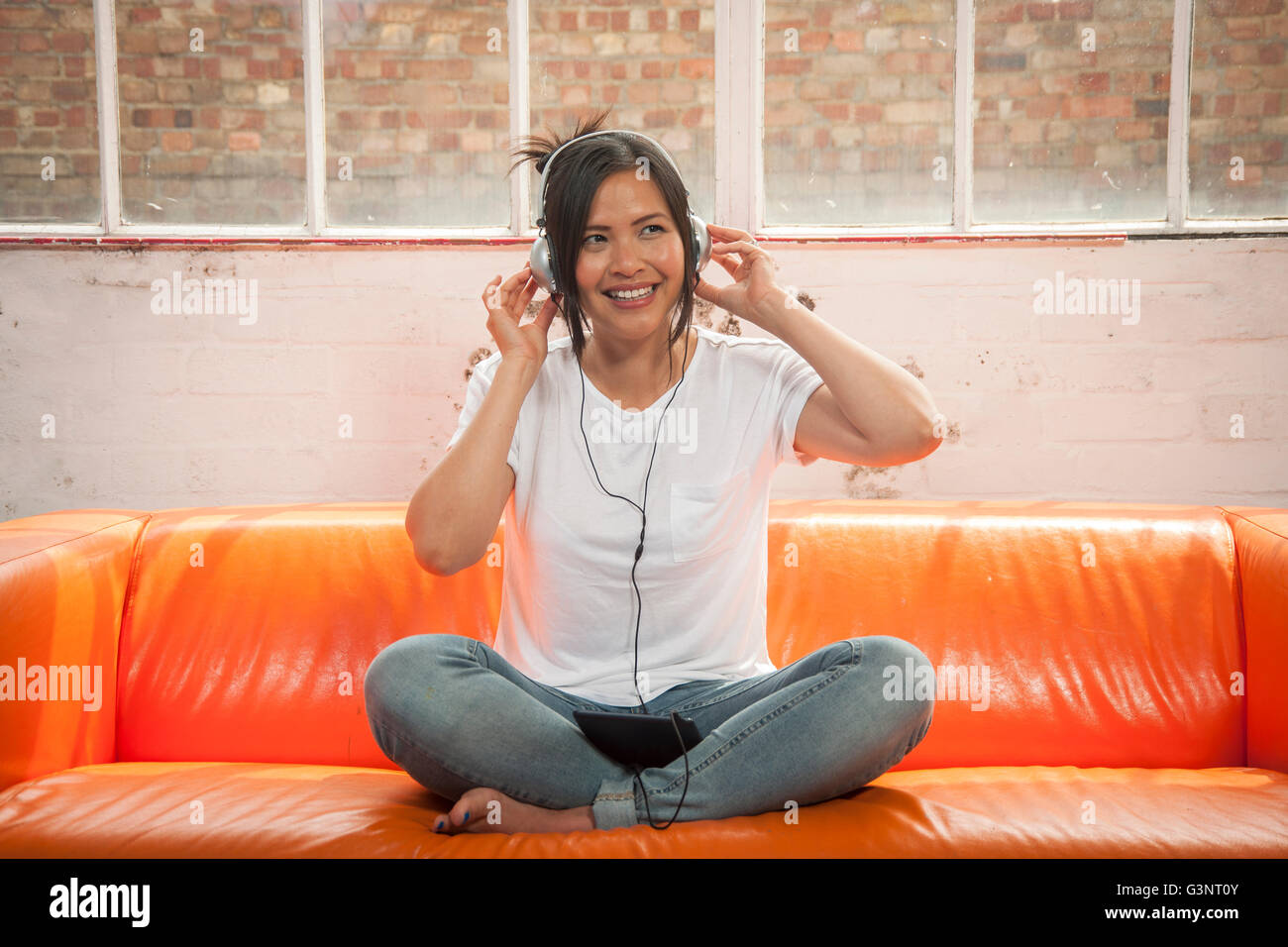 woman sitting crossed legged on a sofa listening to music on headphones on her ipad Stock Photo