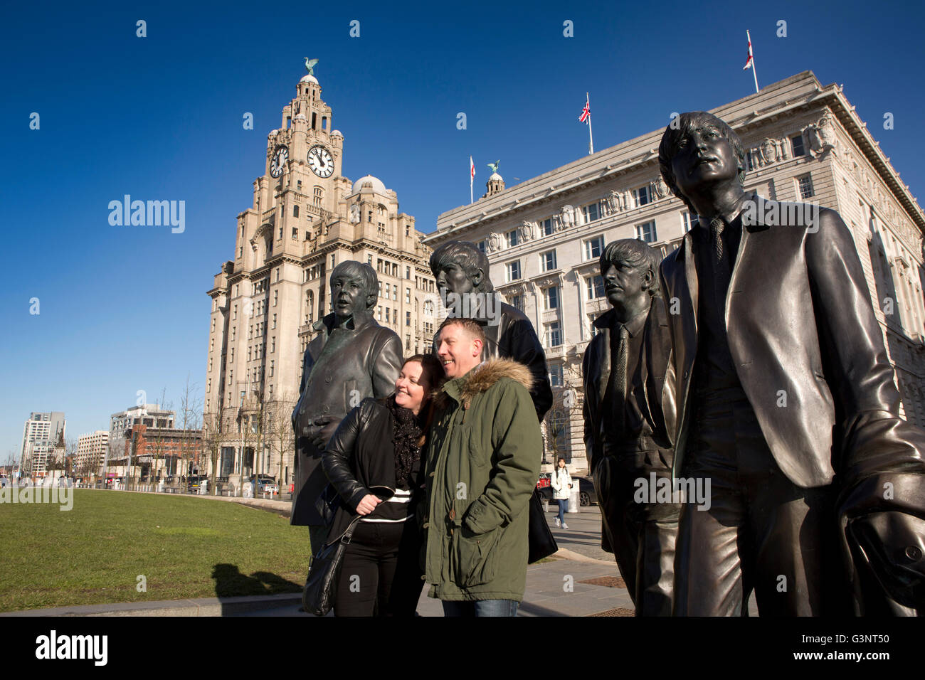 Merseyside, Liverpool, Pier Head, Andrew Edwards’ Beatles statue outside Liver Building, visitors taking souvenir photograph Stock Photo